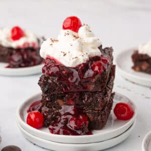 Three black forest brownies stacked on top of each other on a white plate.