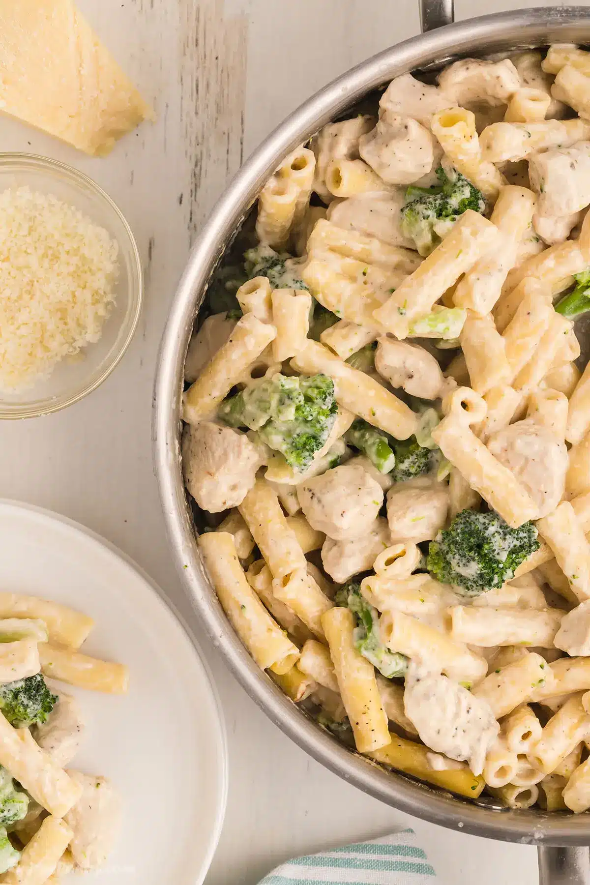 A top view of a pan with creamy chicken broccoli ziti with a parmesan wedge on the side.