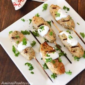 An overhead view of a white plate with chicken kofta garnished with parsley and yogurt sauce.