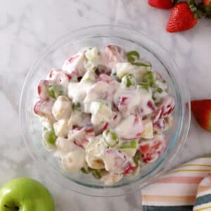 An overhead view of a glass bowl with creamy fruit salad.