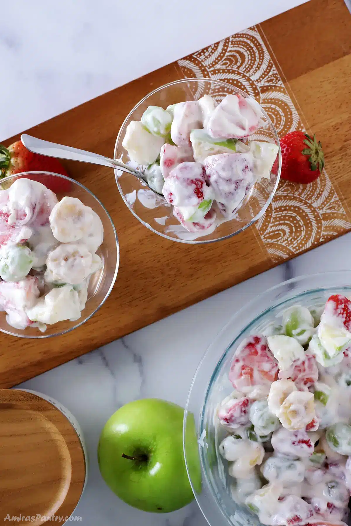 A top view of cups of creamy fruit salad on a wooden board.