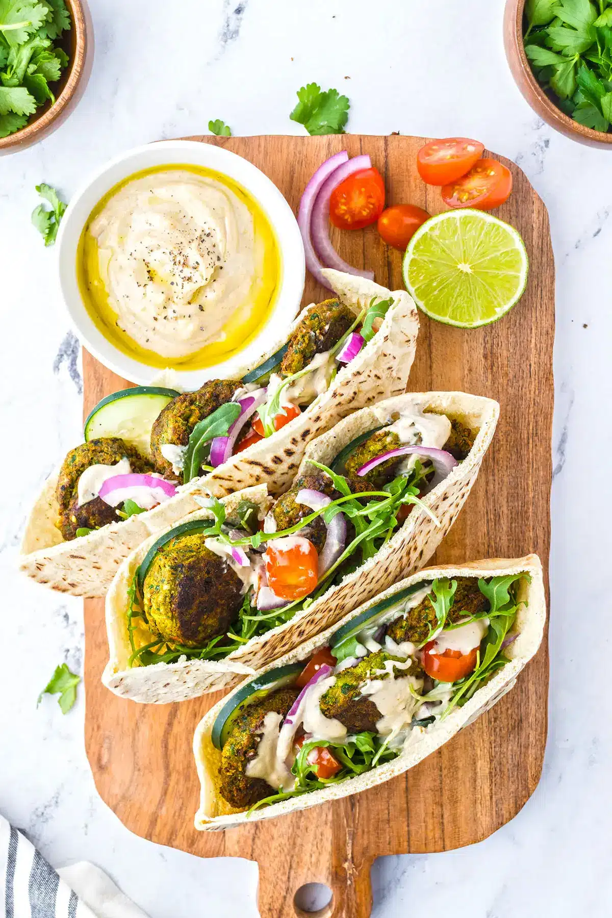 Falafel sandwiches on a wooden serving board with a bowl of tahini on the side.