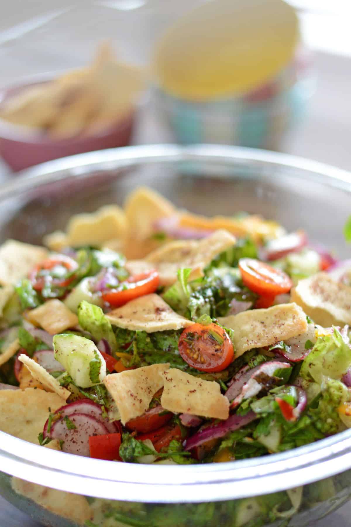 A glass bowl of fattoush salad with small bowls in the back.