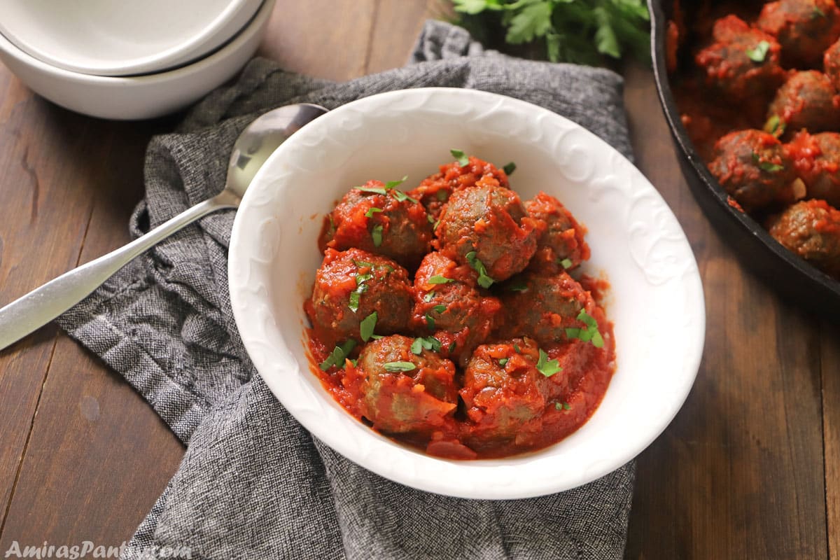 A white bowl with meatballs in tomato sauce.