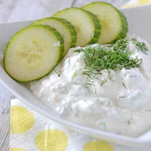 A white triangular shaped plate with tzatziki sauce and some cucumber rings on the side.