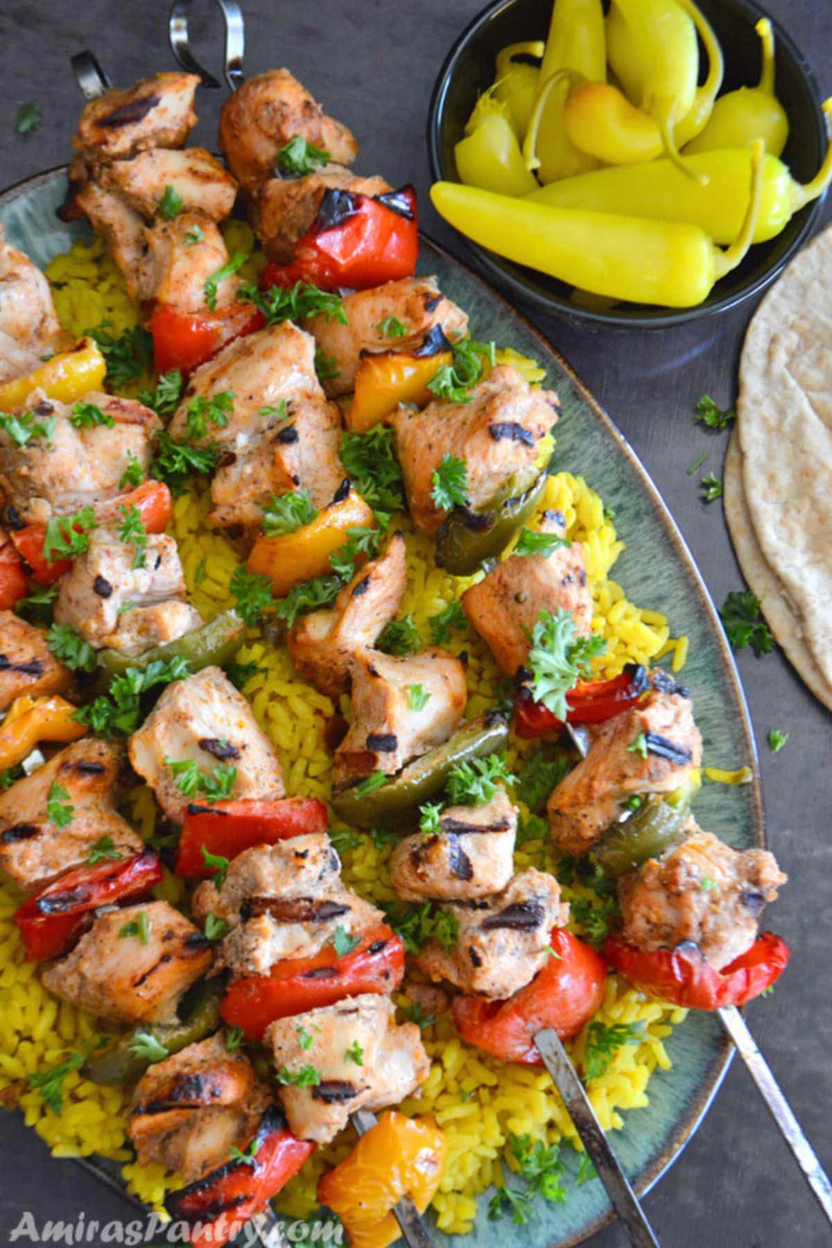 Grilled chicken kabob skewers on a platter over yellow rice.