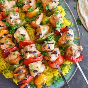 A top view of a platter with chicken kabob skewers on yellow rice.