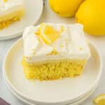 A top view of a piece of lemon poke cake on a white plate with lemon on the back.