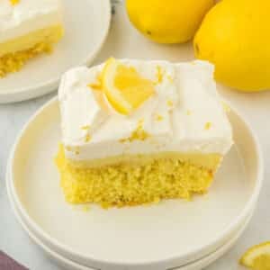 A top view of a piece of lemon poke cake on a white plate with lemon on the back.