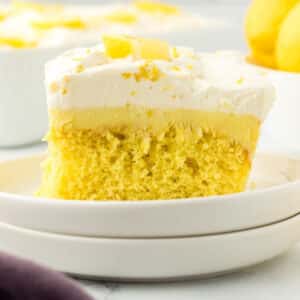 A piece of lemon poke cake garnished with lemon wedges.