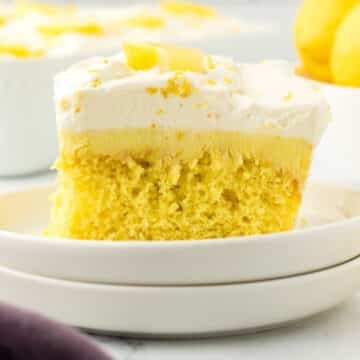 A piece of lemon poke cake garnished with lemon wedges.