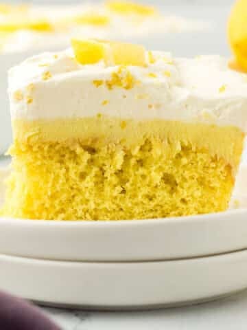 A piece of lemon poke cake garnished with lemon wedges.