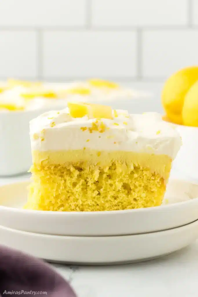 A side view of a piece of lemon poke cake on a white desserts plate.