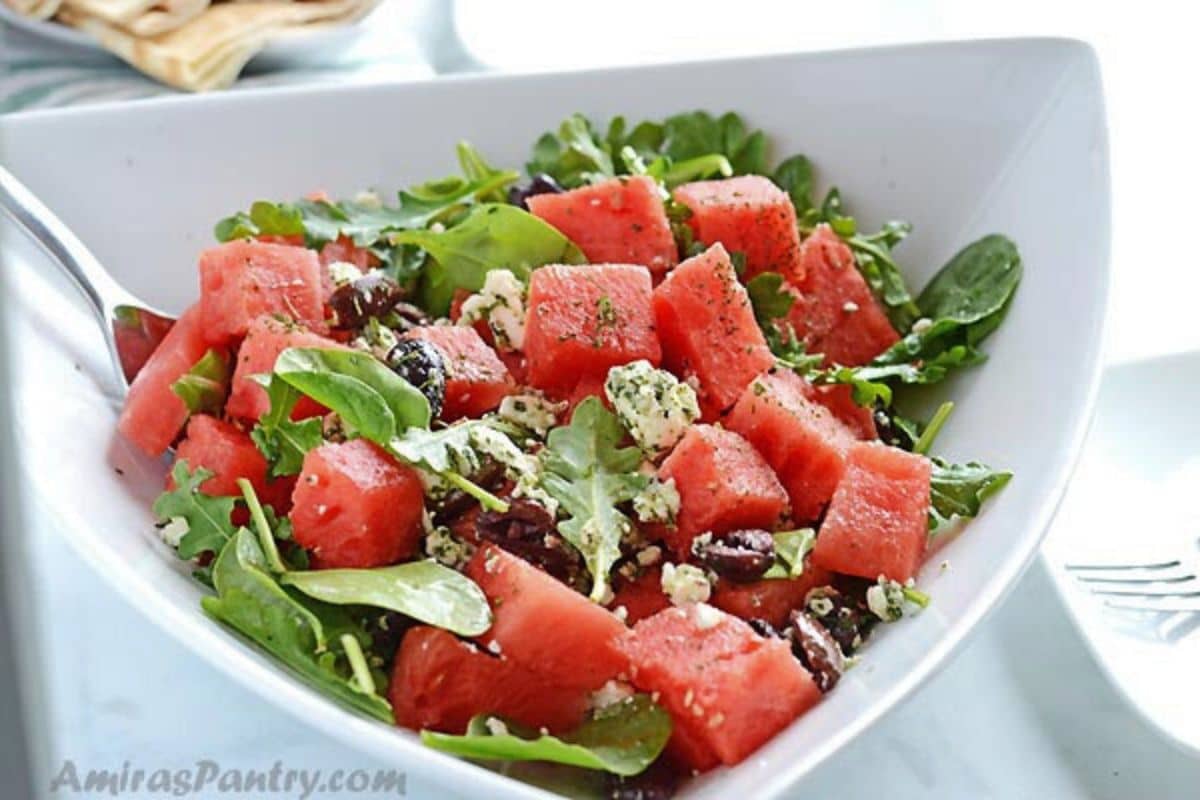 Watermelon arugula salad in a white bowl with a fork in it.