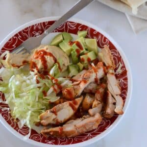 A top view of a plate with baked chicken thighs and some condiments.