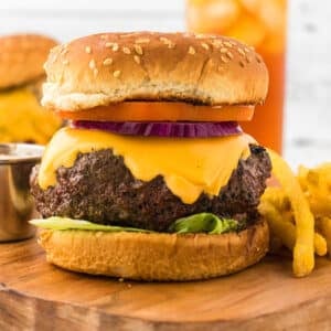 Big Juicy burger on a wooden board with icy cold drink in the back.