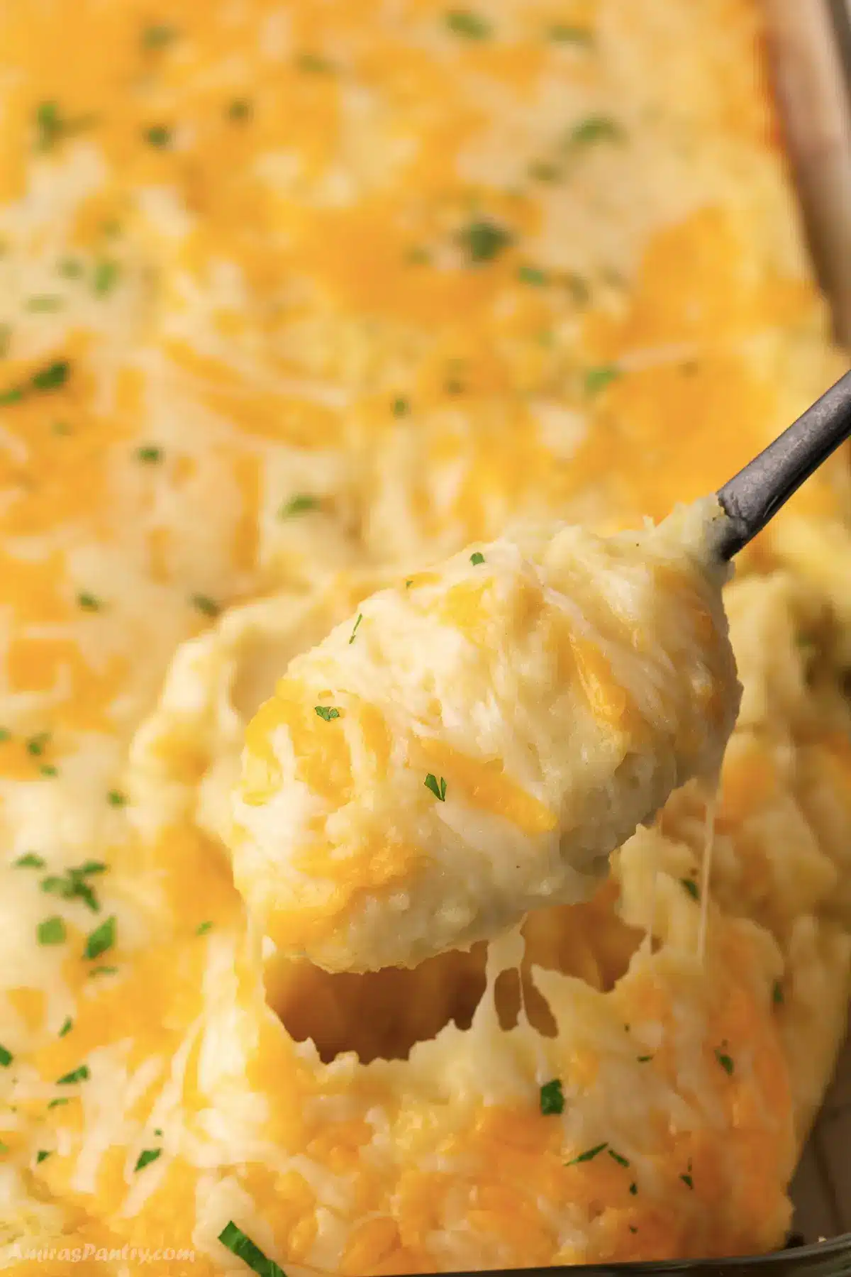 A spoon scooping some cheesy mashed potatoes out of a casserole dish.