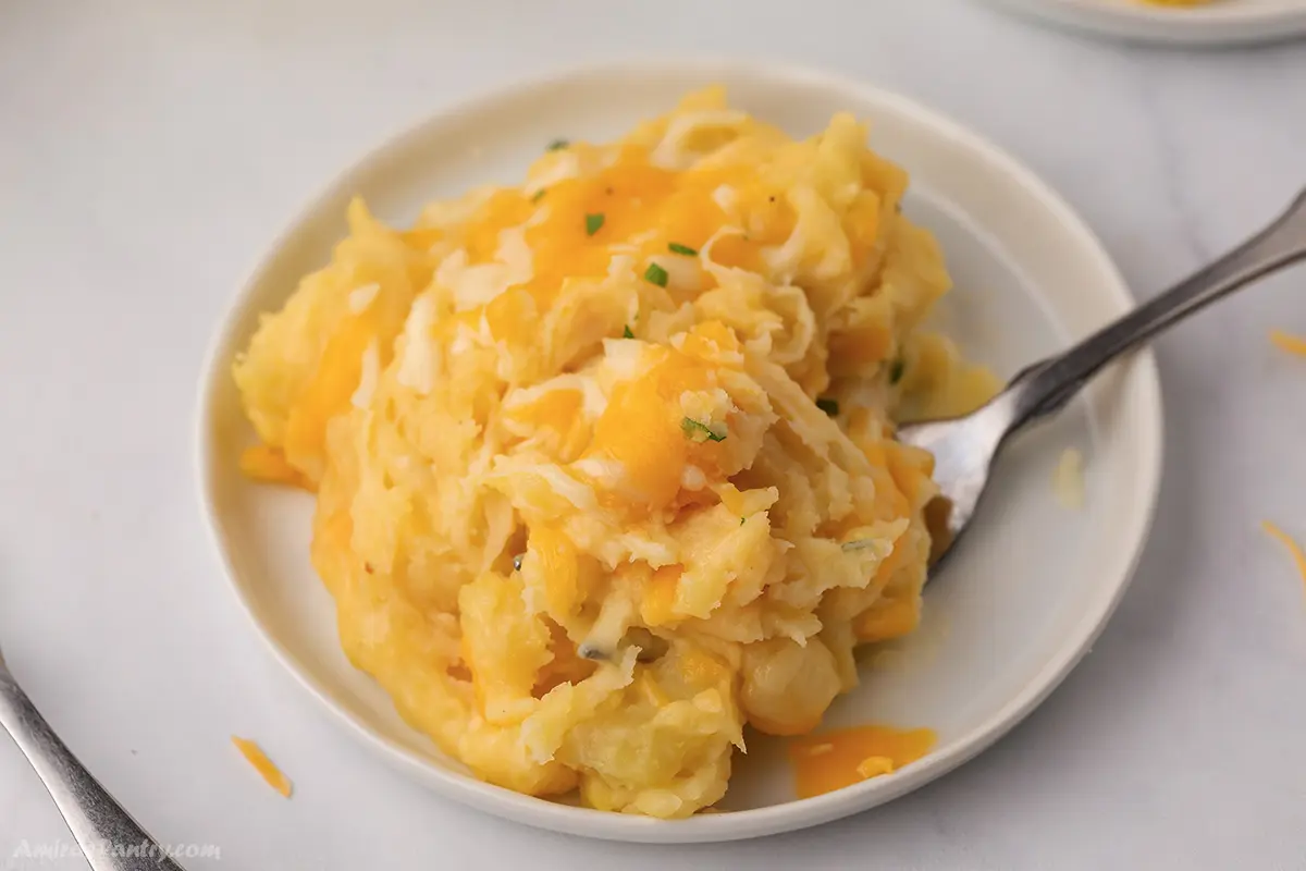 A white plate with some cheesy mashed potatoes with a spoon in it.