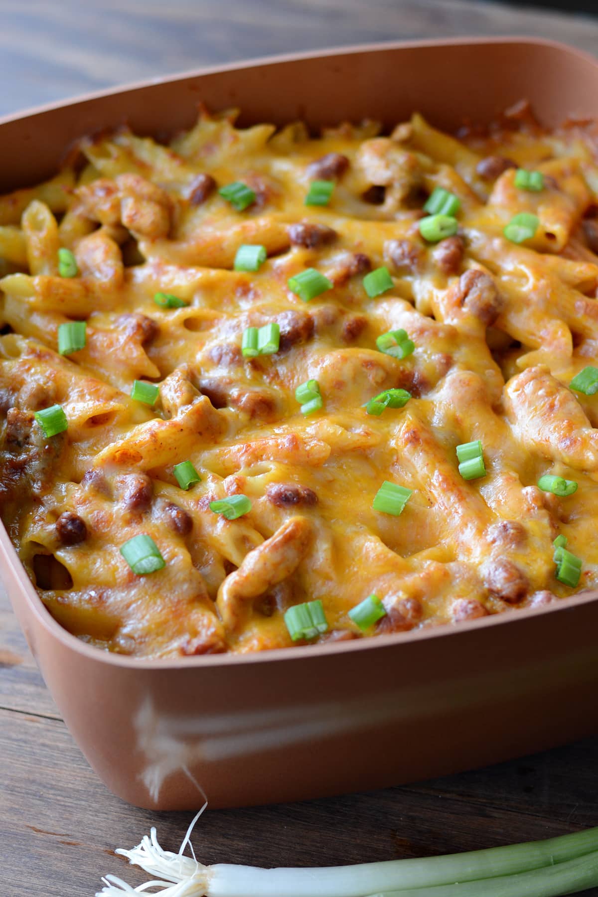 A casserole dish with chicken enchilada pasta garnished with chopped green onion.