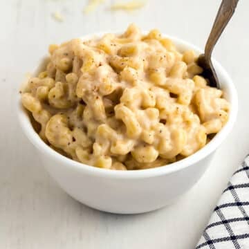A close up image on a bowl with some mac and cheese with a spoon in it.