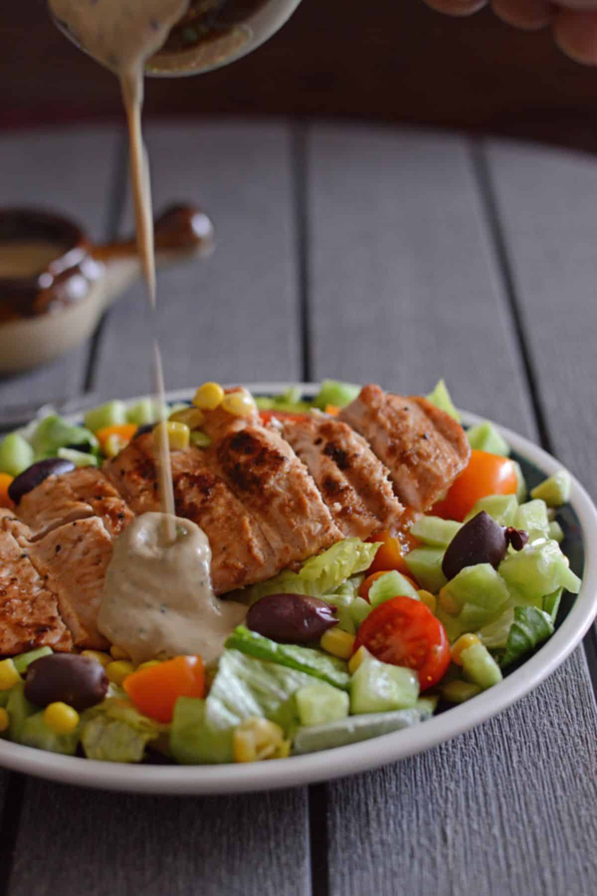 Pouring some kiwi dressing over a plate of grilled chicken salad.