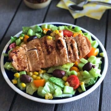 Salad in a plate topped with grilled chicken.