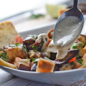 A spoon scooping some tahini yogurt over a bowl of eggplant salad.