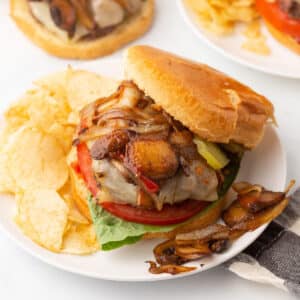 Mushroom Swiss burger sandwich on a white plate with potato chips.