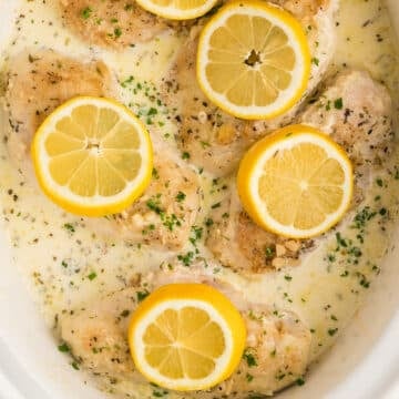 A bird's eye image of part of a slow cooker with creamy chicken garnished with sliced lemons.