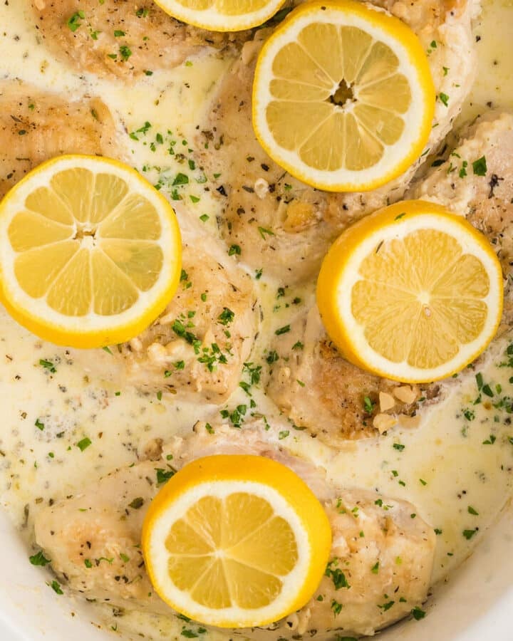 A bird's eye image of part of a slow cooker with creamy chicken garnished with sliced lemons.