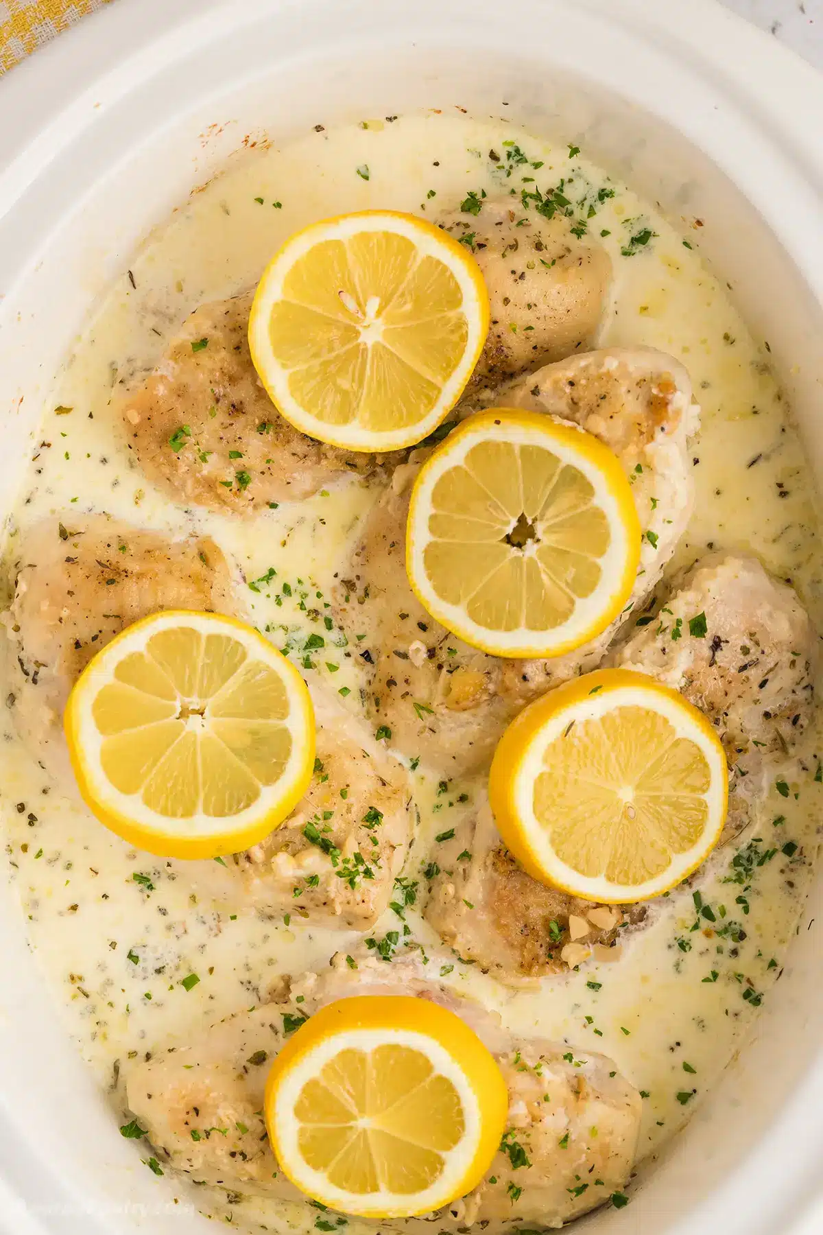 A white slow cooker filled with creamy lemon chicken.
