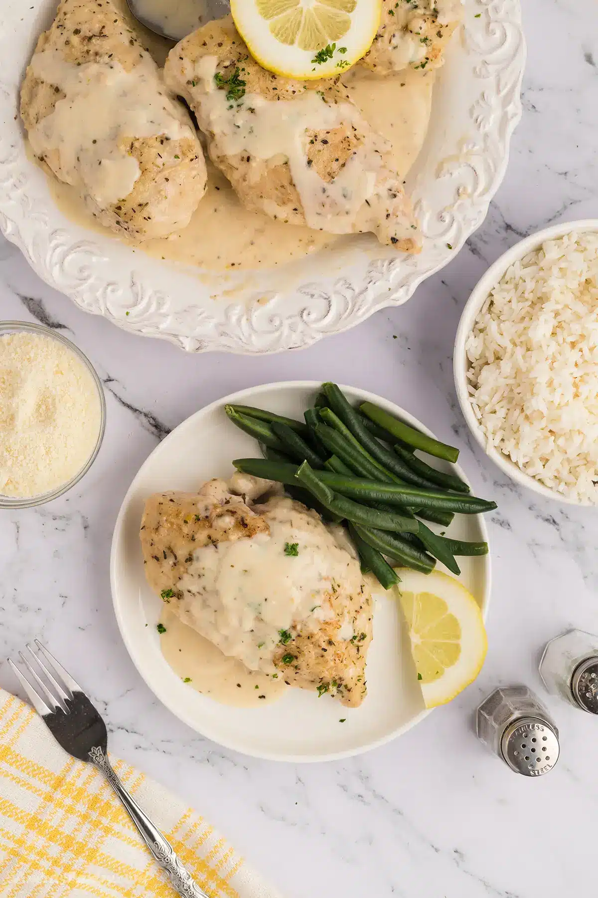 A dinner table with white plates of creamy chicken and green beans.