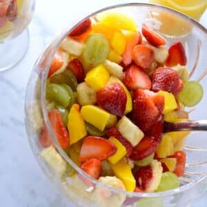 A big glass bowl of fresh fruit salad with a serving spoon.