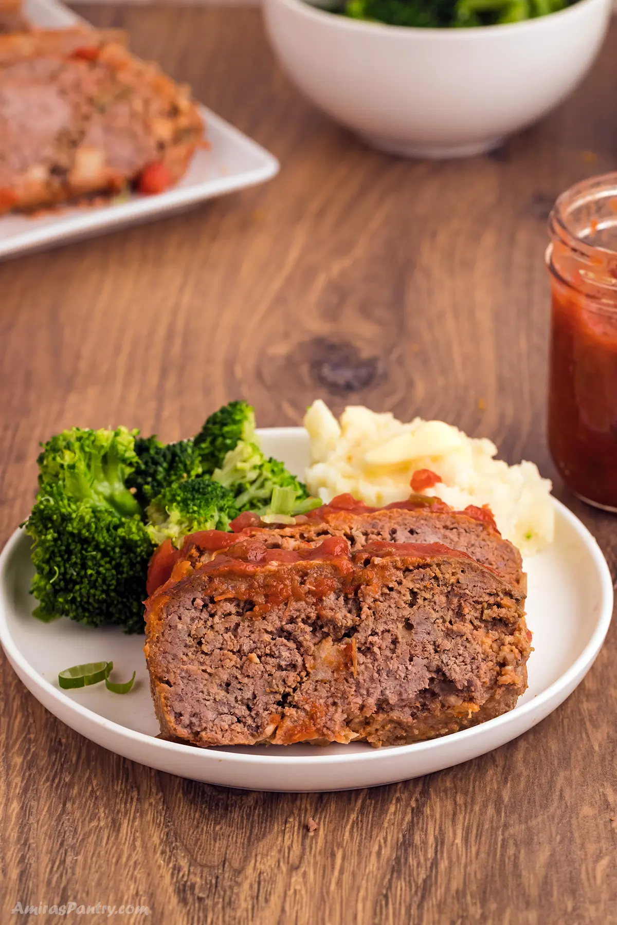 Meatloaf slices on a white plate with broccoli and mashed potatoes.