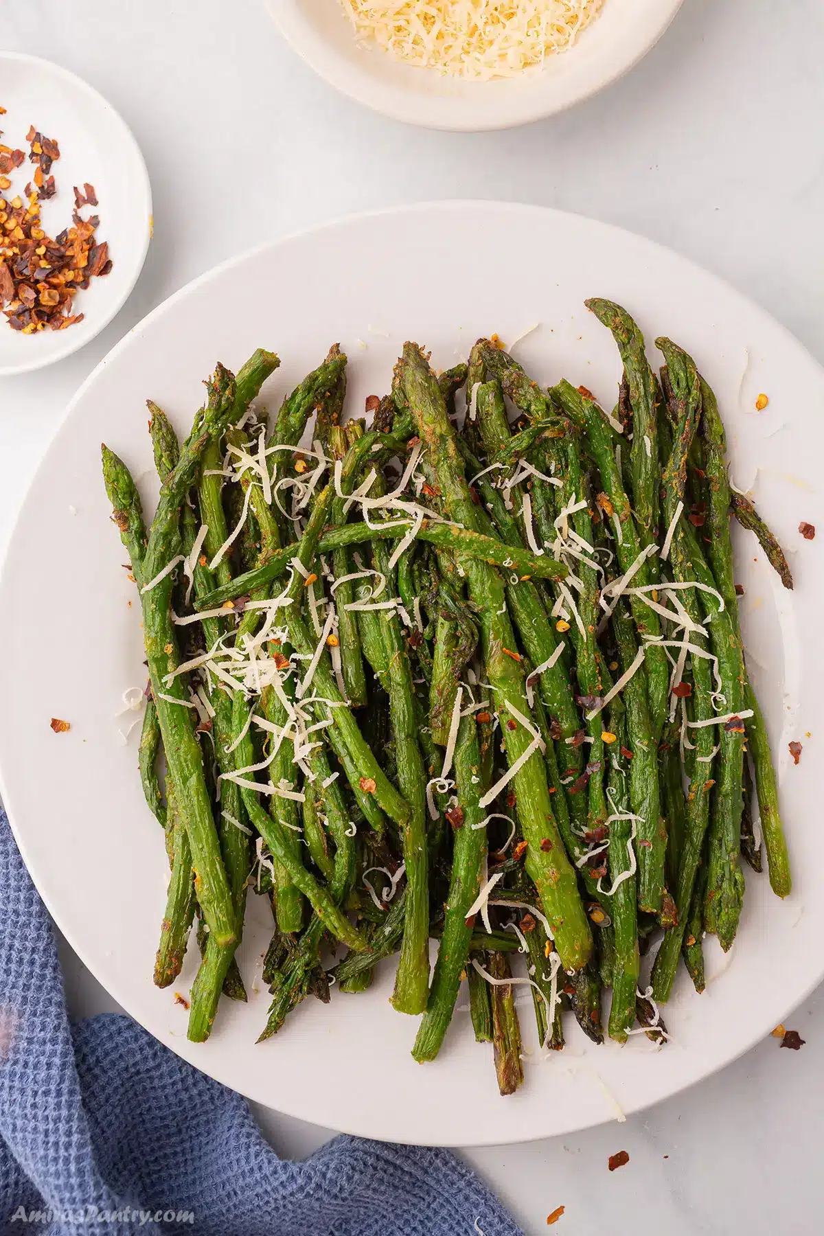 Cooked asparagus in a white plate garnished with parmesan cheese.