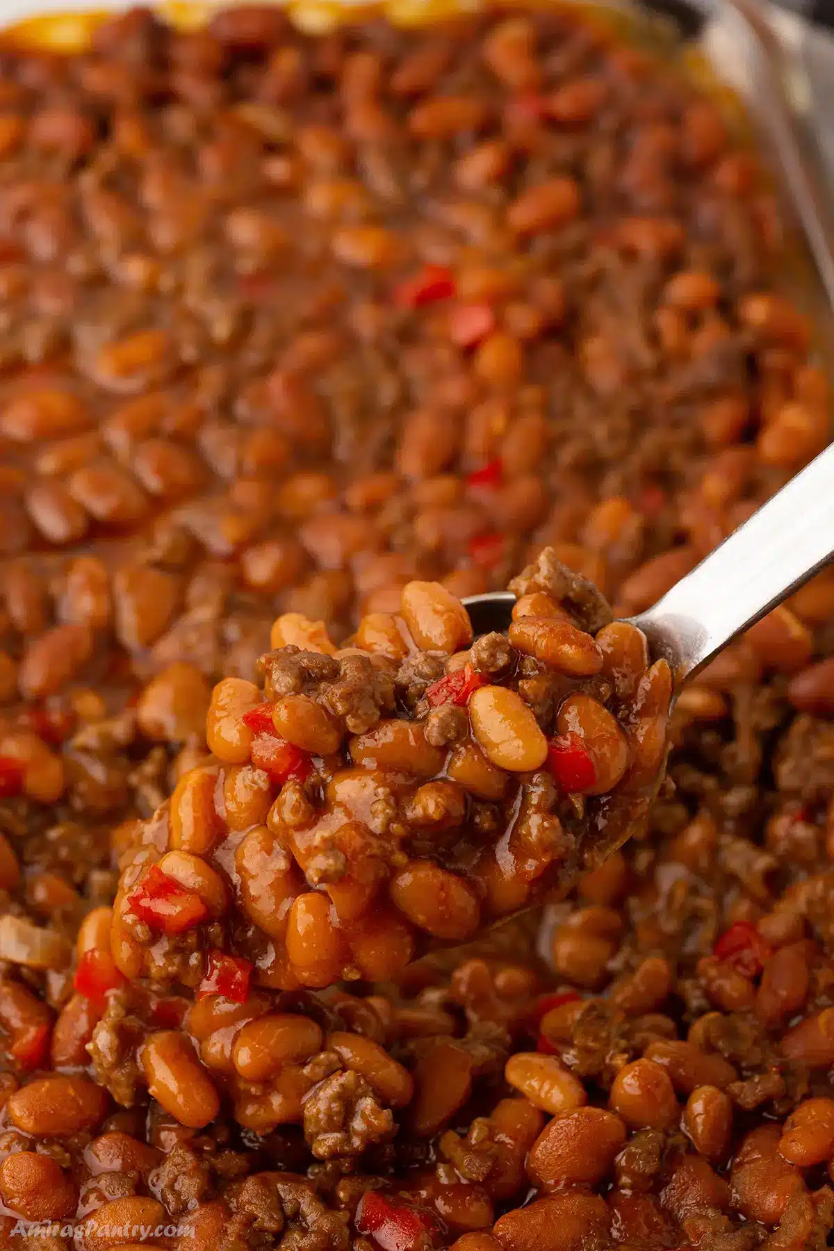 A serving spoon scooping some baked beans with ground beef.