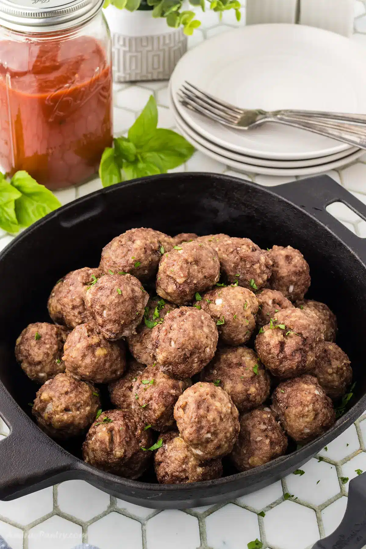 A cast iron skillet filled with meatballs with plates on the back.