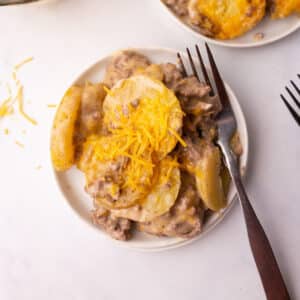 A serving of hamburger potato casserole on a white plate with a fork on the side.