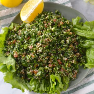 An overhead view of a plate of tabouli salad with lemon wedges on the side.