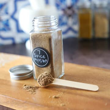 A glass jar with arabic spices on a wooden cutting board.