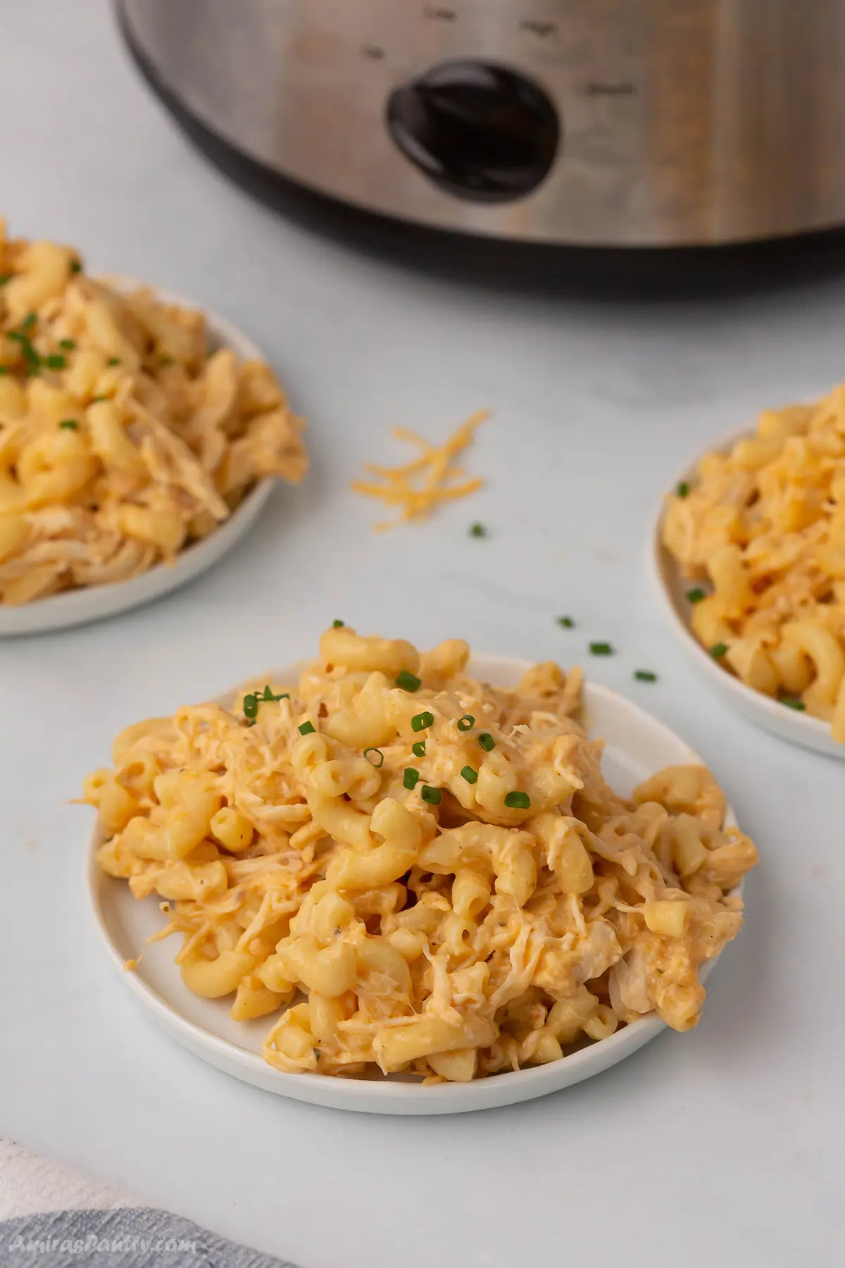 Three plates with buffalo chicken mac and cheese servings with the crockpot in the back.