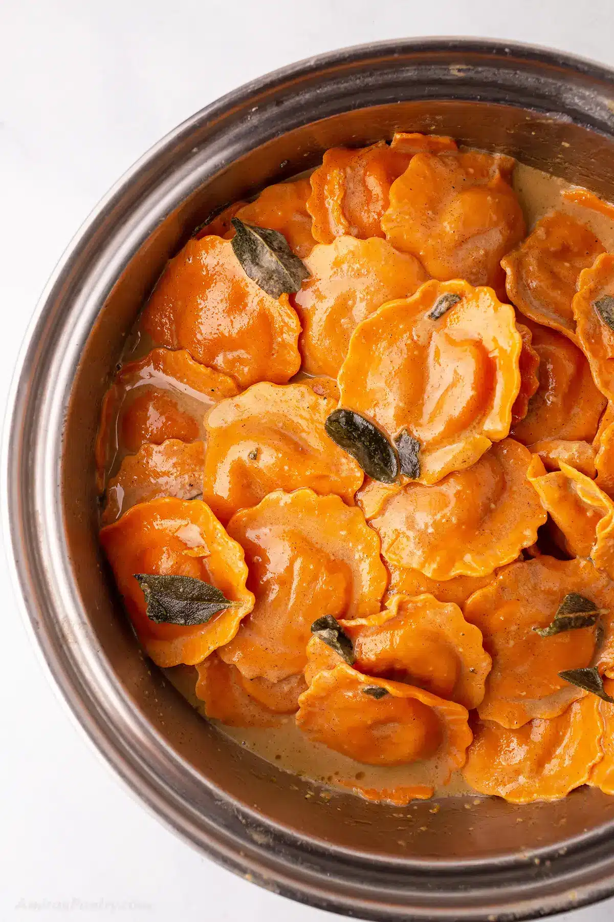 A bowl with butternut squash ravioli with sauce and sage on the top.