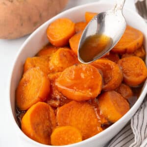 A spoon drizzling some sauce over candied sweet potatoes.