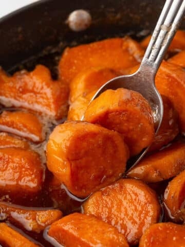 A spoon scooping some candied sweet potato out of a big skillet.
