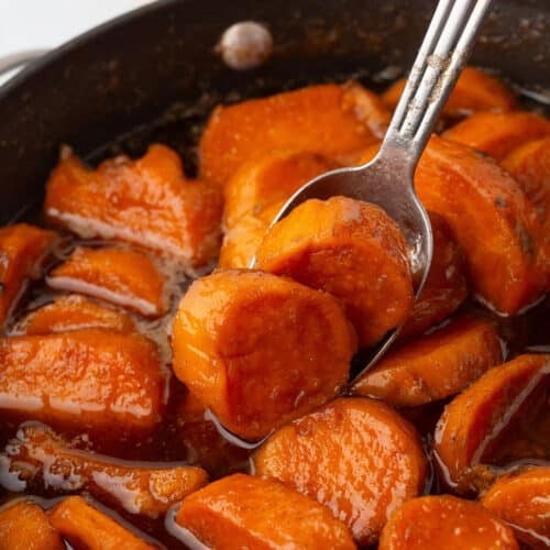 A spoon scooping some candied sweet potato out of a big skillet.
