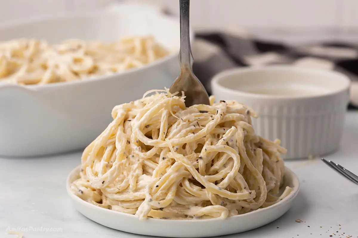 A closeup of a serving of cream cheese pasta on a white dish.