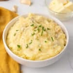 Zoomed in image of a white bowl with mashed potatoes garnished with parsley.
