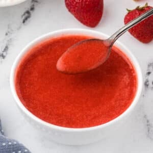 Strawberry coulis in a white bowl with a spoon.
