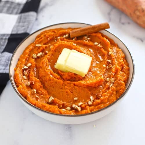 A top view of a bowl with whipped sweet potatoes garnished aith butter and nuts.