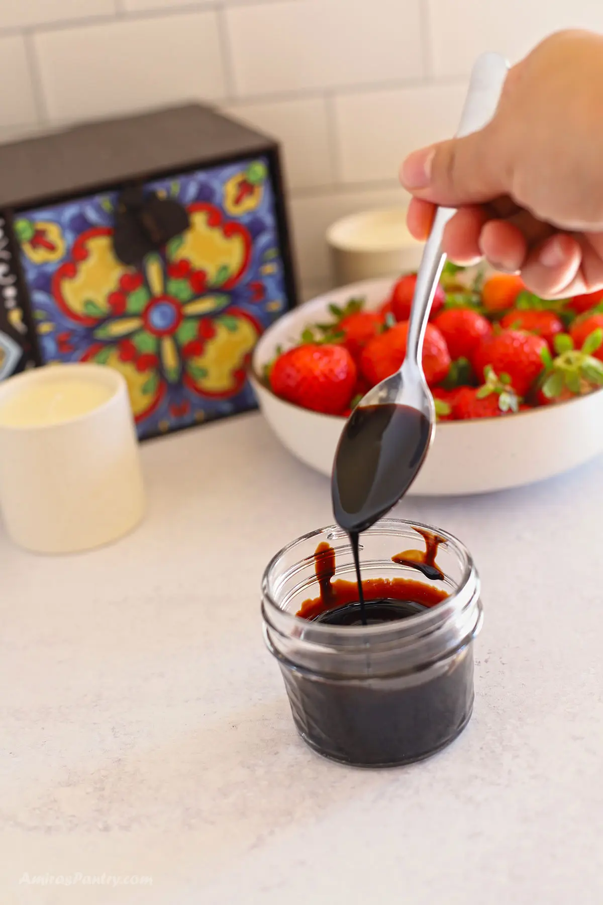 A spoon with some honey balsamic glaze over a jar.